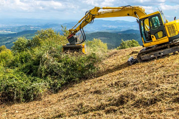 Excavator with a FEMAC mulcher clearing a steep slope
